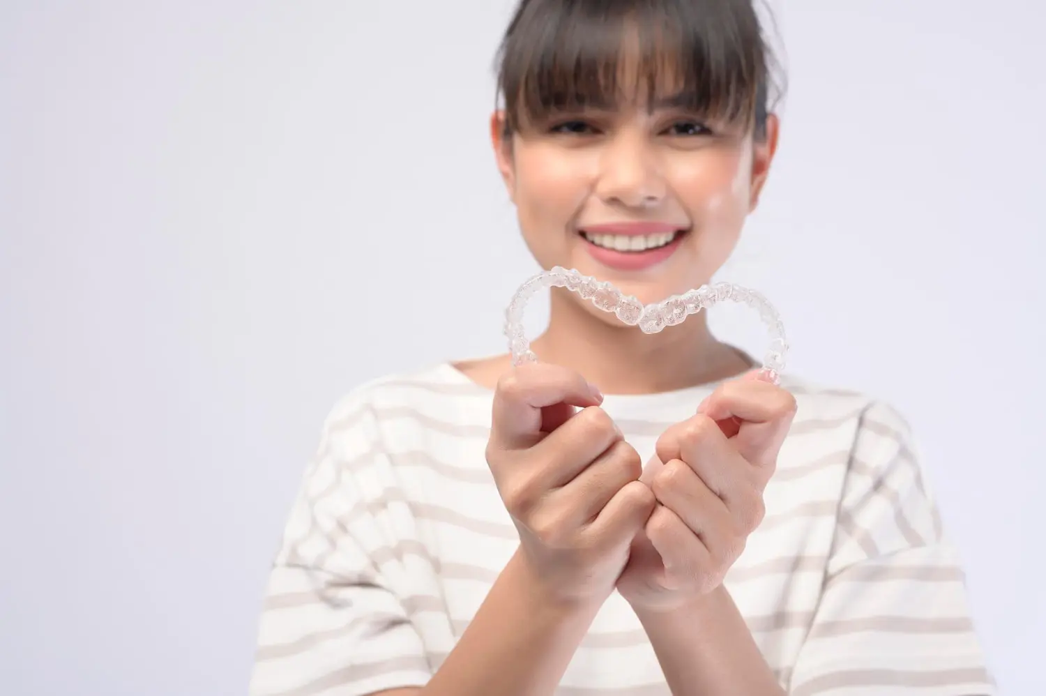 A person in a striped shirt smiles broadly, showcasing clear dental aligners, a testament to the best orthodontics innovation, against a plain background.