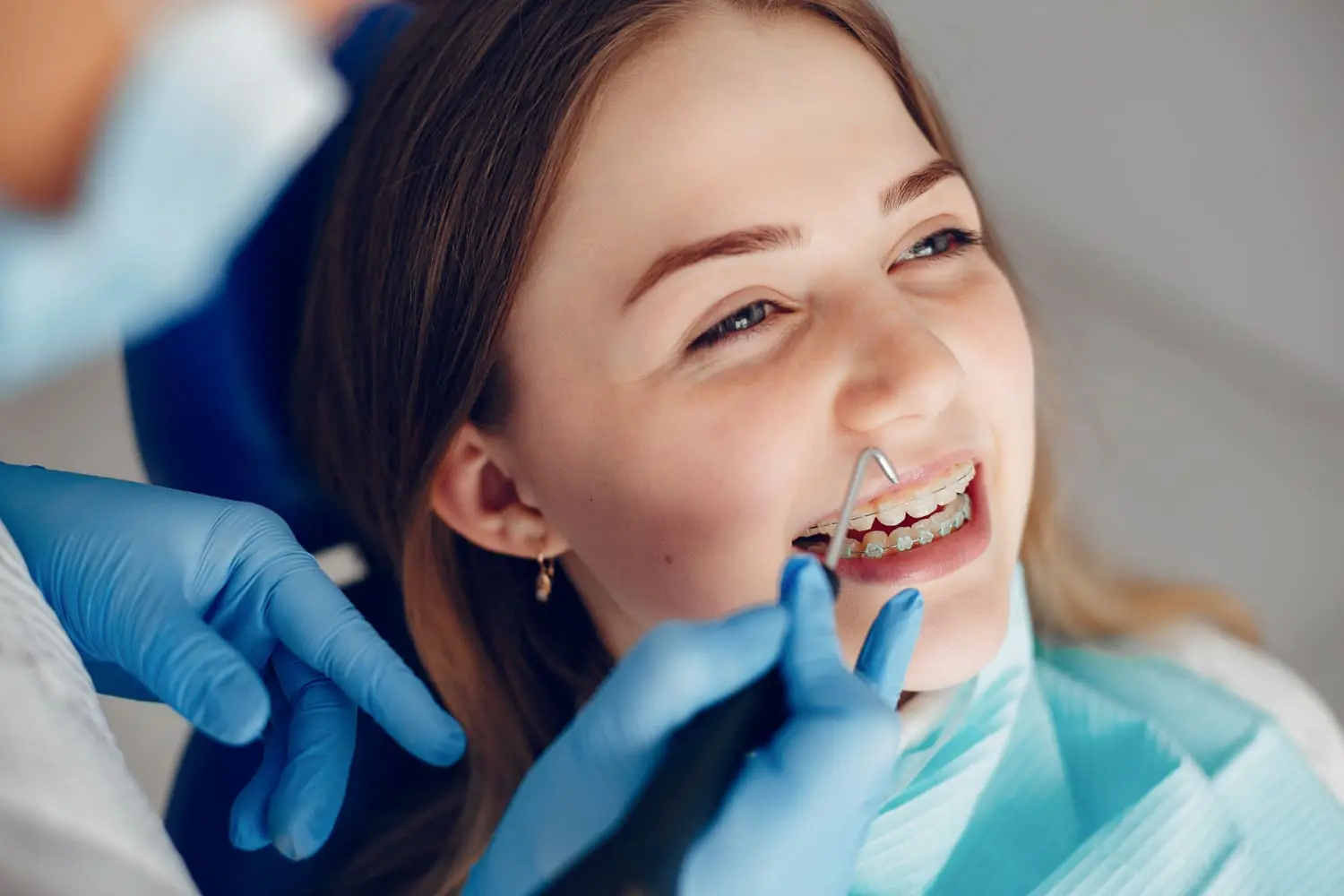 Person with braces receiving a dental checkup at Best Orthodontics. The dentist, wearing blue gloves, expertly uses dental tools.