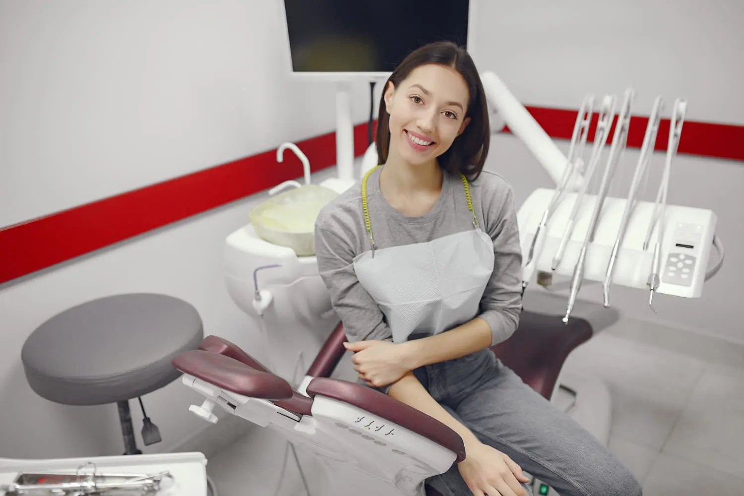 A woman sits in a dental chair, her smile glowing at Best Orthodontics. Behind her, state-of-the-art dental equipment and a monitor attest to the advanced care she receives.