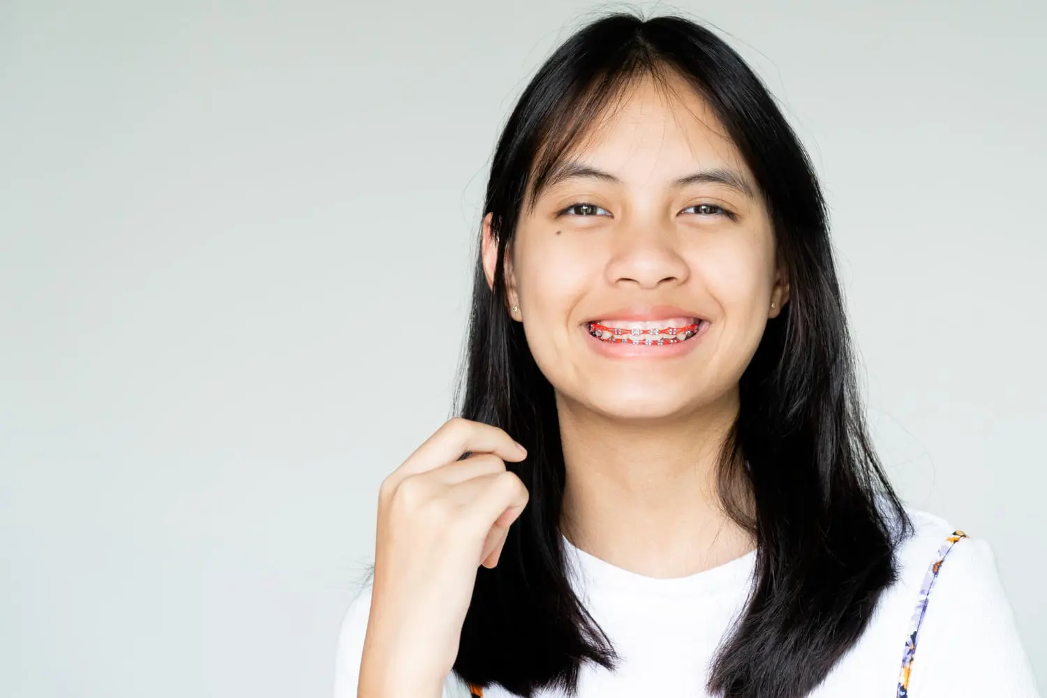 A young woman with long black hair beams brightly, her braces a testament to the craftsmanship of the Best Orthodontics team.