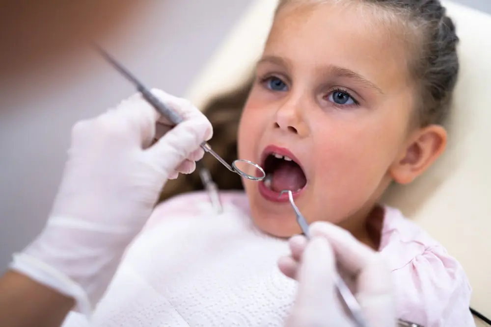 Young girl in a dental chair having her teeth examined by a dentist using a dental mirror and probe.