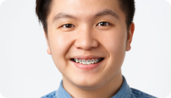 A person with braces smiles at the camera, wearing a denim shirt.