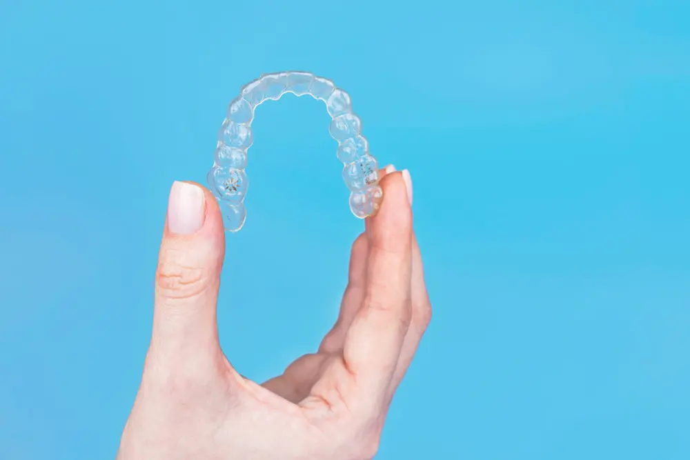 A hand holds Invisalign clear aligner against a blue background.