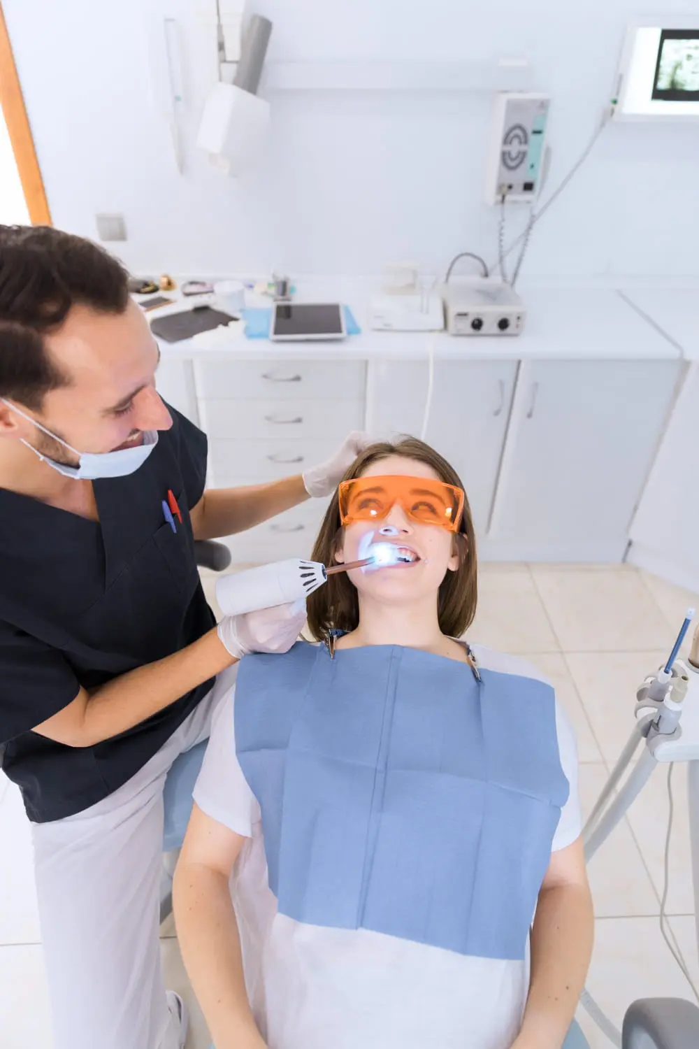 At the best orthodontics clinic, a dentist skillfully performs a teeth whitening procedure on a patient wearing orange protective glasses, ensuring bright and confident smiles.
