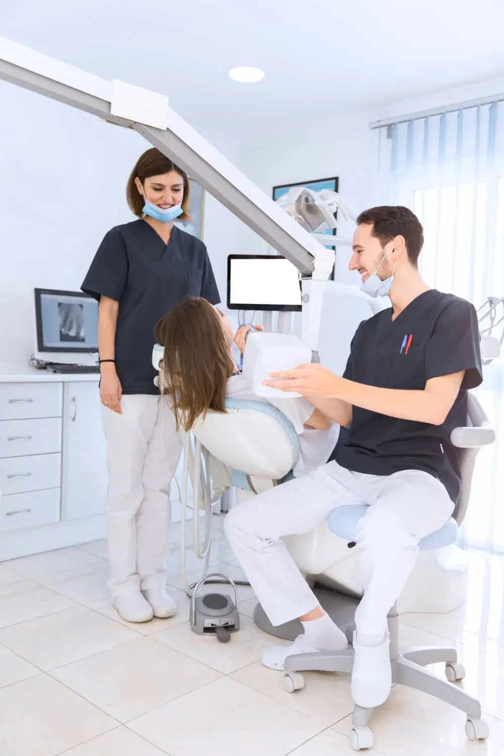 A dentist and assistant from Best Orthodontics carefully examine a patient in a dental chair, surrounded by state-of-the-art dental equipment and a computer screen displaying essential data.