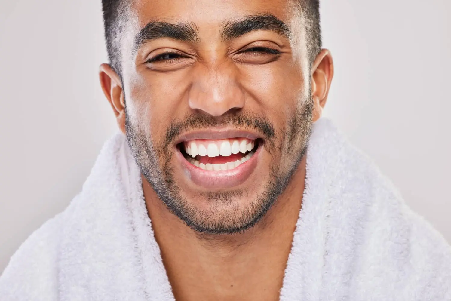 Close-up of a person smiling warmly, revealing the stunning results of the best orthodontics, wearing a white towel around their shoulders.