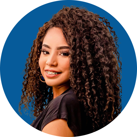 Woman with long curly hair, wearing a black top and adult braces, smiling against a blue background.