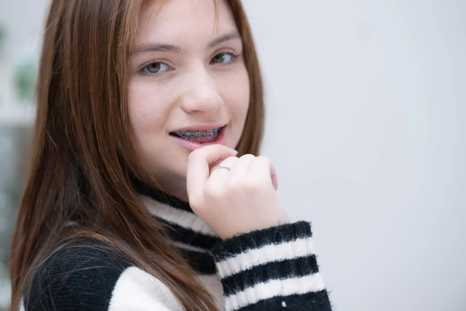 A person with long hair and braces from Best Orthodontics wears a black and white striped sweater, looking at the camera with a slight smile.
