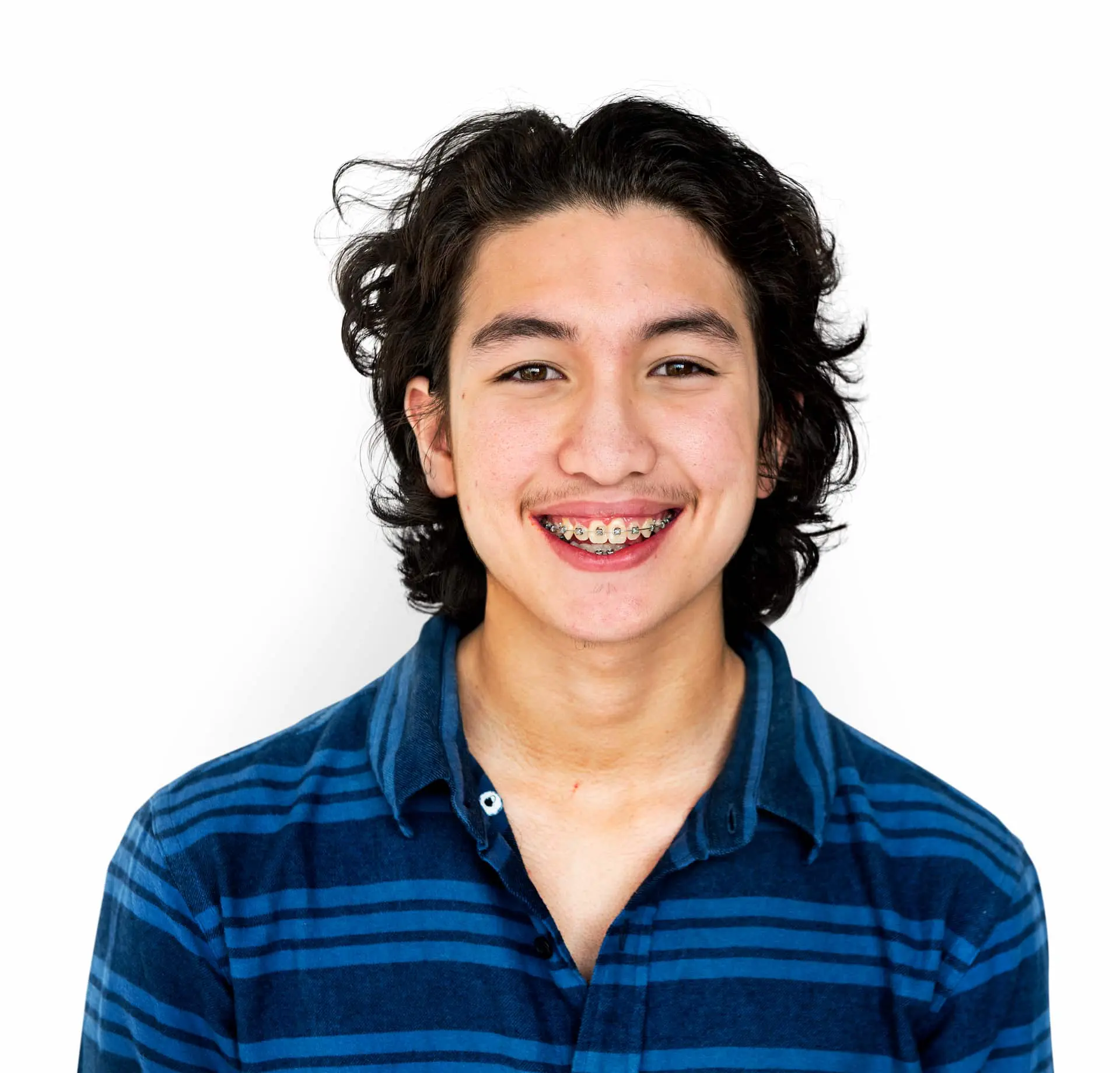 An adult with long curly hair and braces, wearing a blue and black striped shirt, smiles warmly against a white background in Austin and Houston