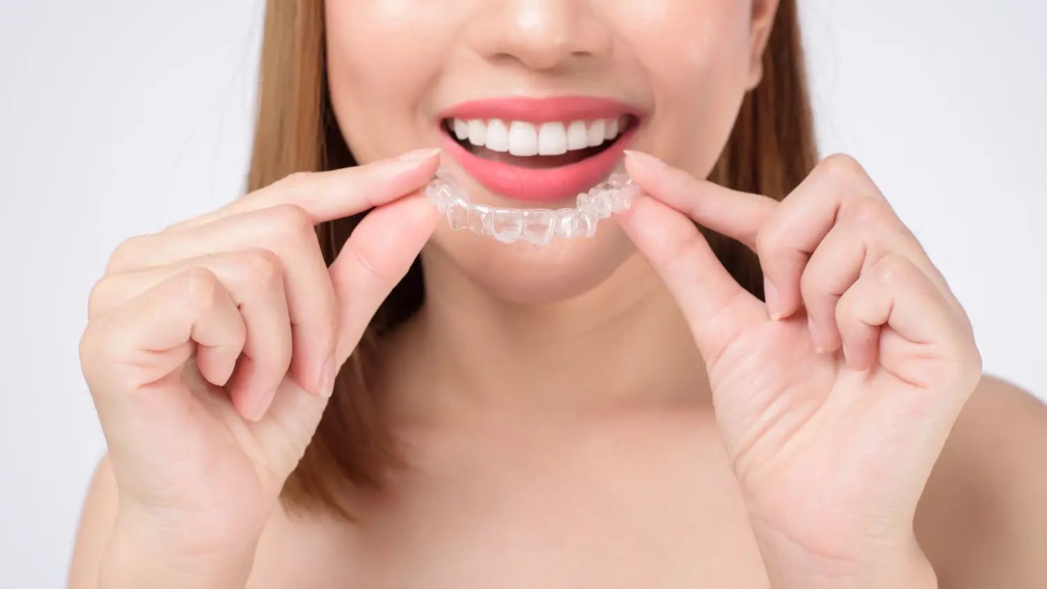A person proudly showcases their best orthodontics achievement by holding a clear dental aligner near their smiling mouth.