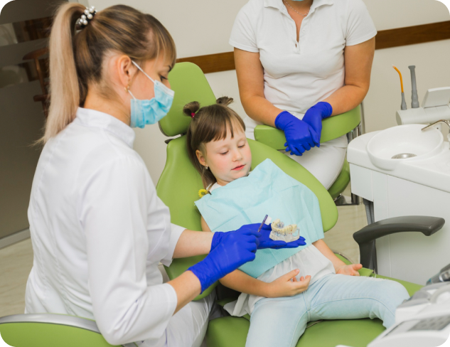 Dentist showing a dental mold to a child sitting in a dental chair while an assistant looks on.